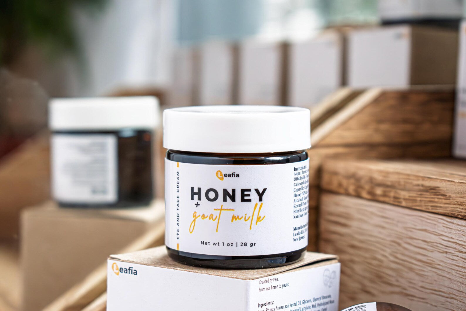 Leafia Skincare honey goat milk face and eye cream jar with white lid on wooden boxes in warm apothecary setting
