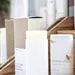 Sweet Almond Oil lotion sticks in white twist-up tubes displayed on natural wood blocks with soft light and minimal apothecary styling.