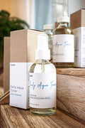 Leafia Skincare Daily Aqua Toner in clear glass bottle on wooden surface with additional bottles and packaging in background