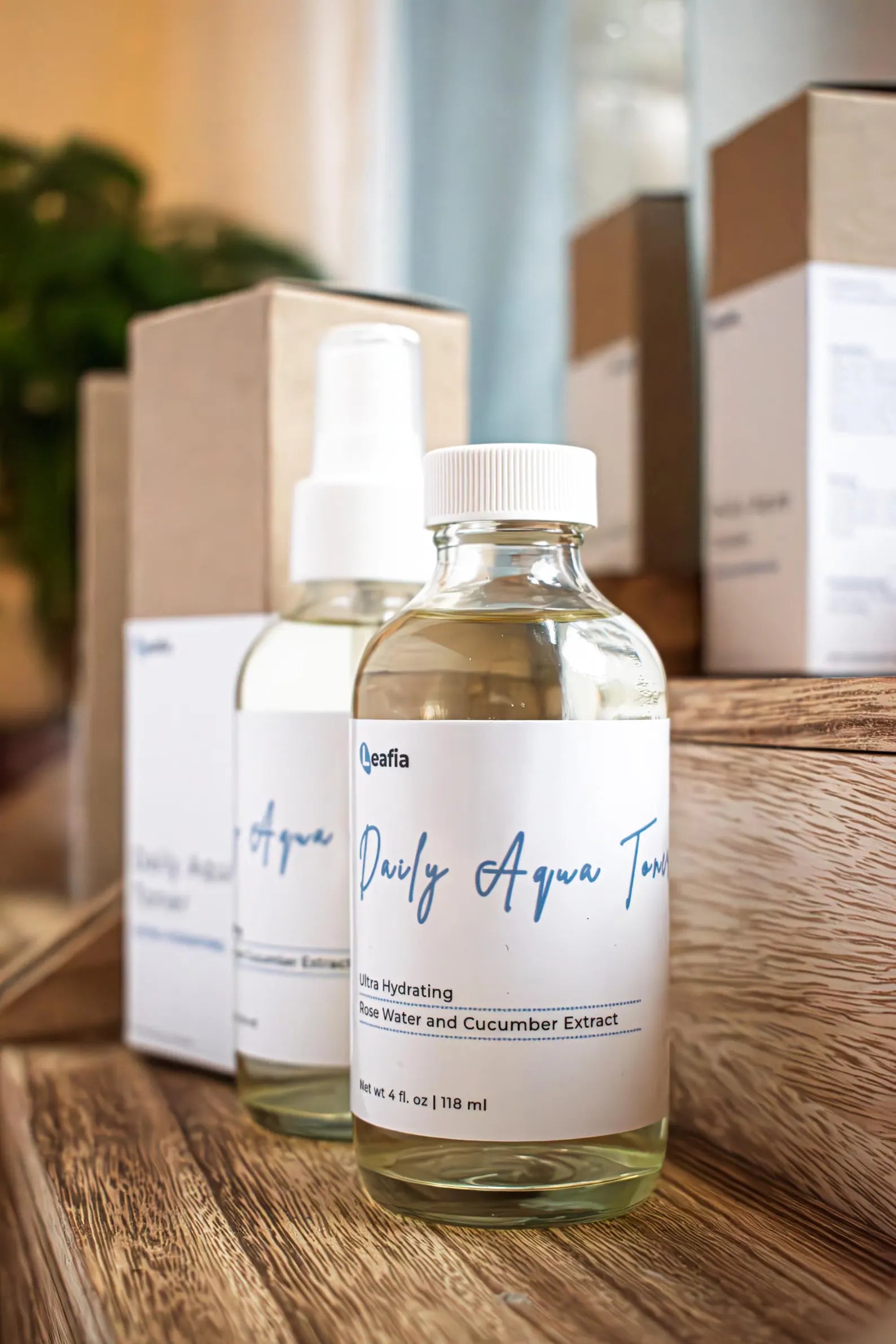 Leafia Skincare Daily Aqua Toner in clear glass bottle on wooden steps beside packaging with other toner bottles behind