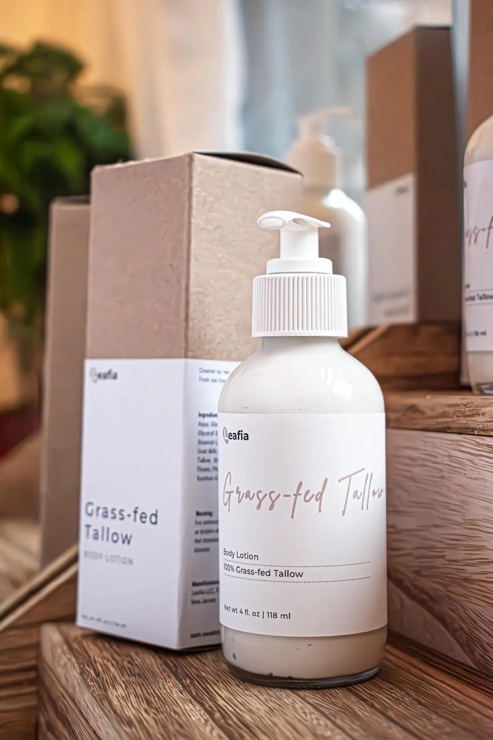 Leafia Skincare grass-fed tallow body lotion in white pump bottle on wooden steps beside matching kraft box