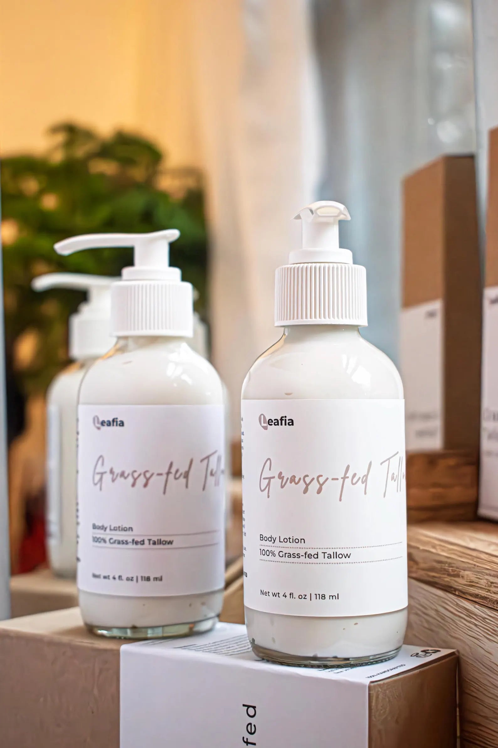 Leafia Skincare grass-fed tallow body lotion creamy daily moisturizer in clear pump bottles on wood blocks with soft neutral light