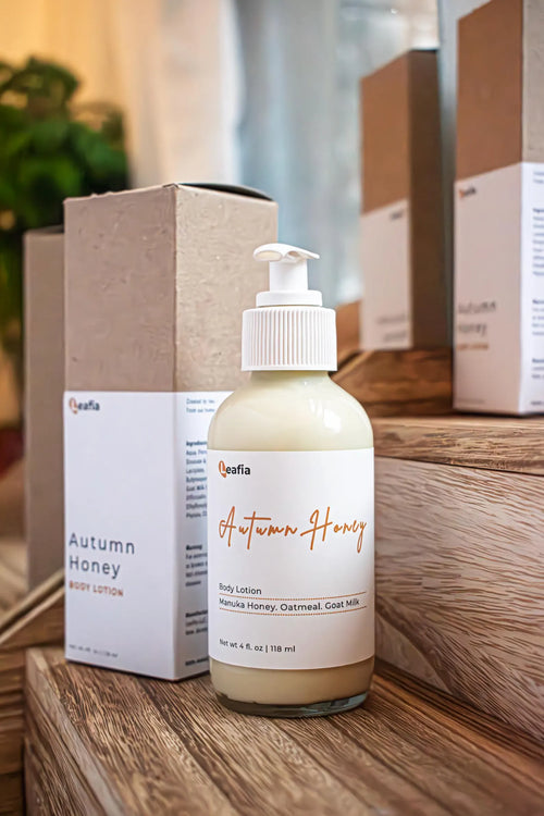 Leafia Skincare honey oat body lotion in clear pump bottle on wood blocks with matching box in natural skincare setting
