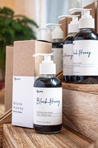 Leafia Skincare Black Honey charcoal cleanser exfoliating honey gel face wash in dark glass pump bottles on wood blocks, soft apothecary light