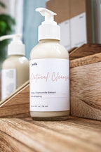 Leafia Skincare Oatmeal Cleanser gentle cream facial cleanser in clear pump bottle, angled close-up with soft apothecary light