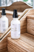 Leafia Skincare Green Tea Face Lotion in clear glass pump bottle on wooden steps with soft natural light