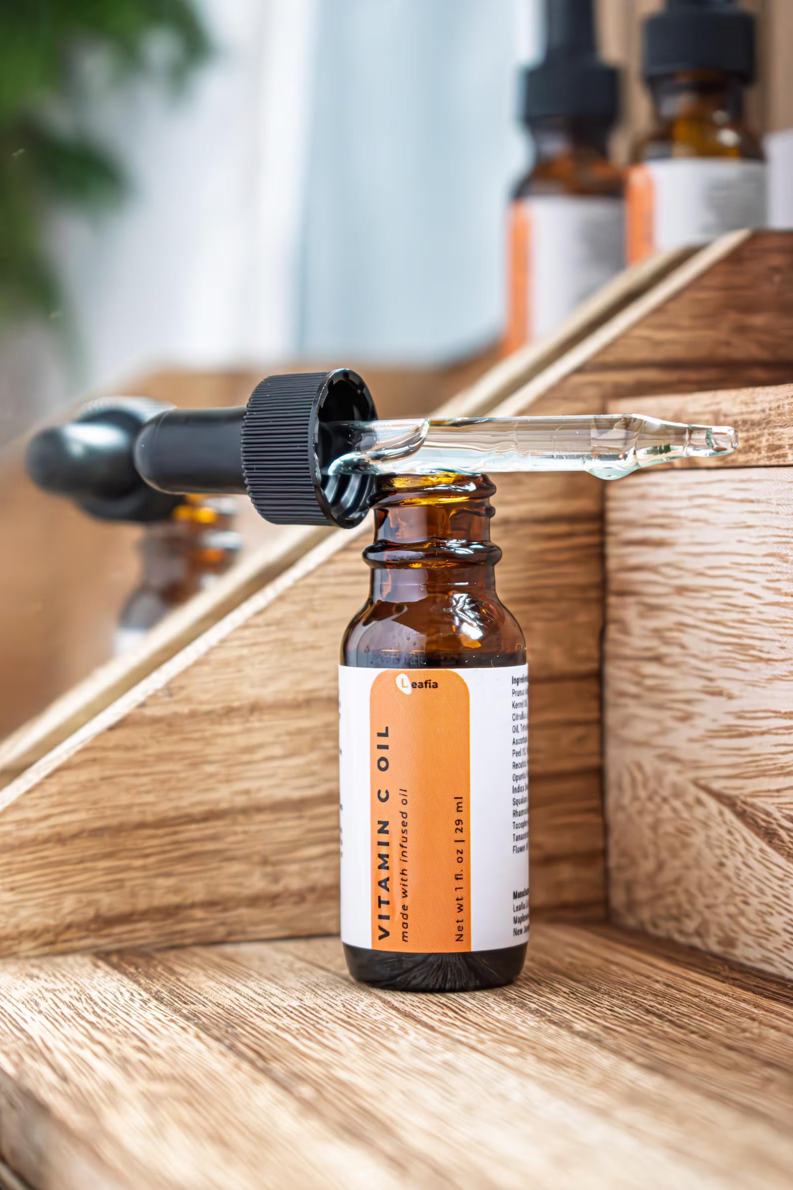 Leafia Skincare Vitamin C facial oil in glass dropper above amber bottle, soft light with minimal apothecary styling