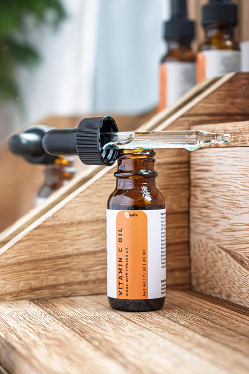 Leafia Skincare Vitamin C facial oil in glass dropper above amber bottle, soft light with minimal apothecary styling