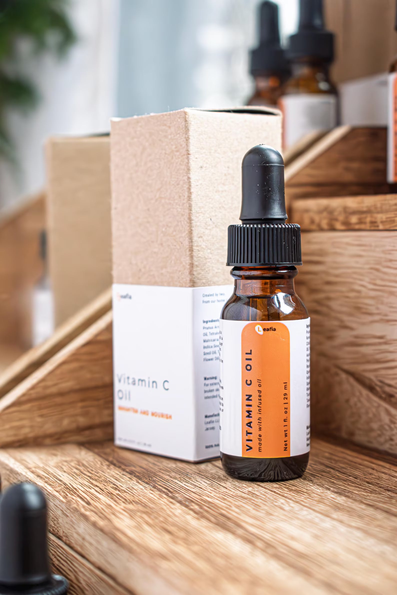 Leafia Skincare Vitamin C facial oil in amber dropper bottle beside kraft box on rustic wooden shelves