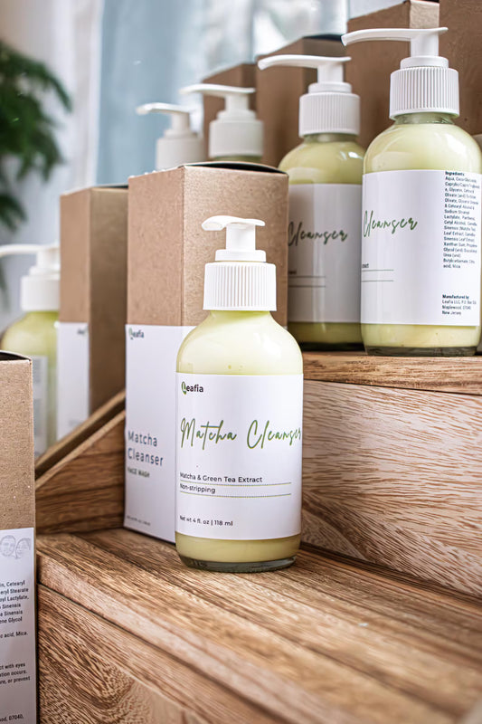 Leafia Skincare Matcha Green Tea facial cleanser in clear pump bottle with matching boxes on wooden shelves in soft natural light