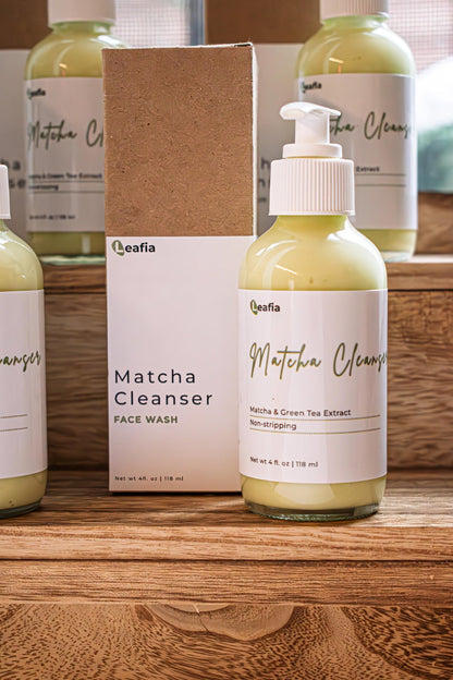 Leafia Skincare Matcha Green Tea gentle cream cleanser in clear pump bottle on wood blocks, soft apothecary light