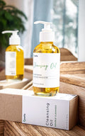 Leafia Skincare cleansing oil in clear pump bottle with golden oil on white box atop rustic wood in natural light