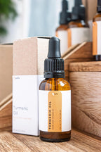 Leafia Skincare turmeric infused facial oil in amber glass dropper bottle on wooden shelf with minimalist packaging, lightweight jojoba oil skincare