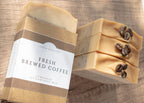 Handmade soap bar with coffee beans and a visible label on a wooden surface