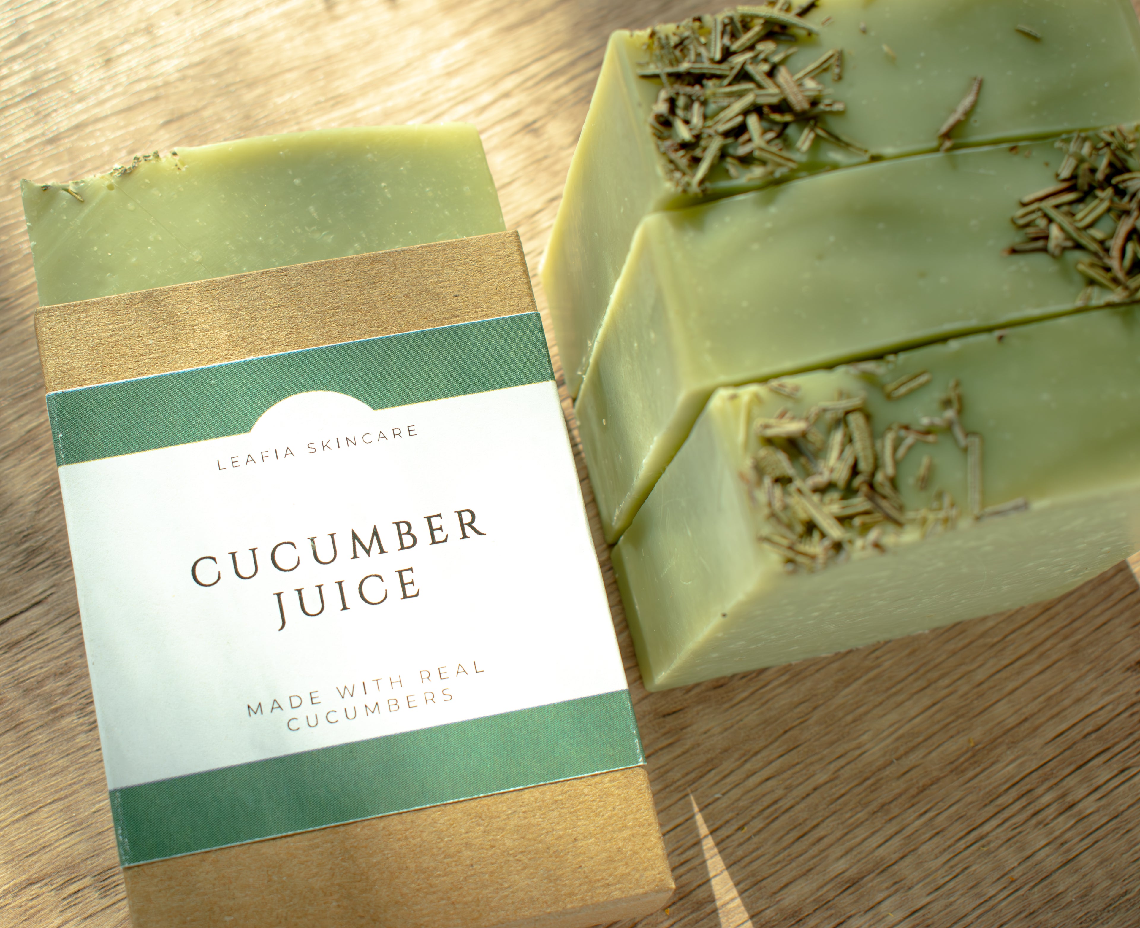 Two bars of cucumber juice soap with a packaging label on a wooden surface