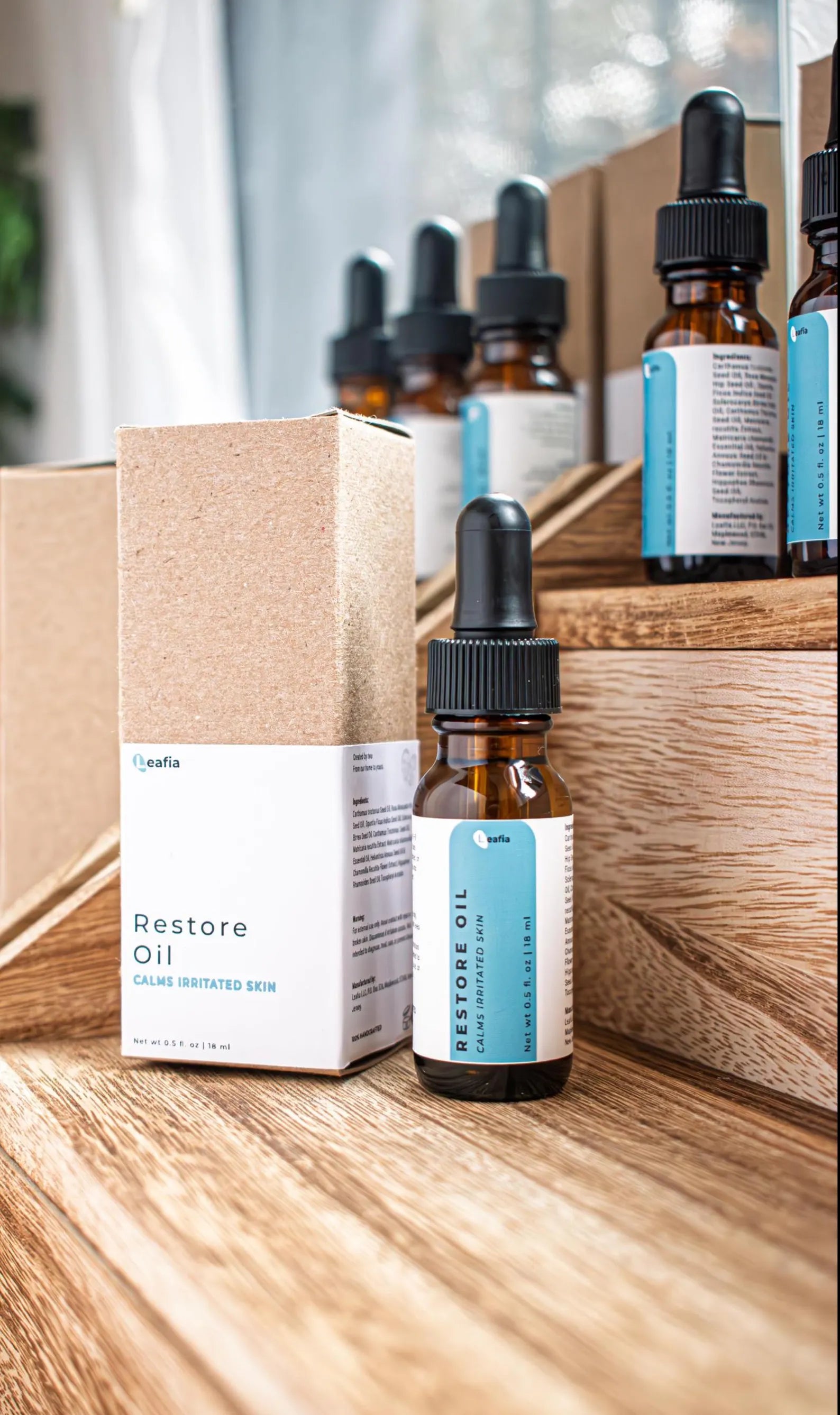Leafia Skincare Restore Oil facial oils in amber glass dropper bottles on natural wood blocks with soft light