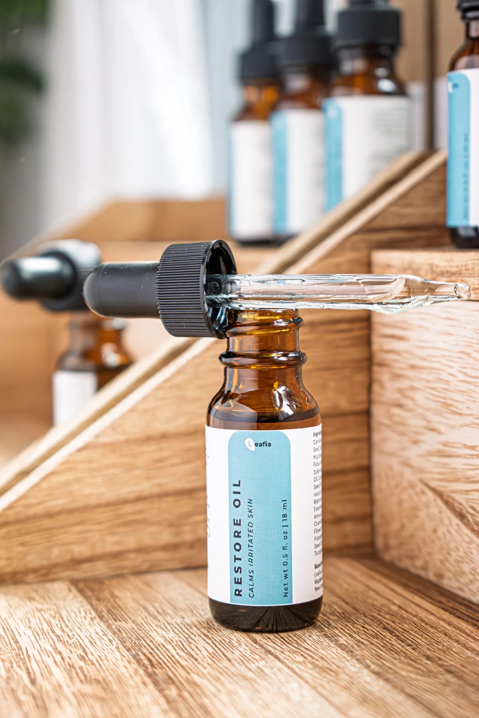 Leafia Skincare Restore Oil facial oil in amber dropper bottles on wood blocks, soft light and minimal apothecary styling