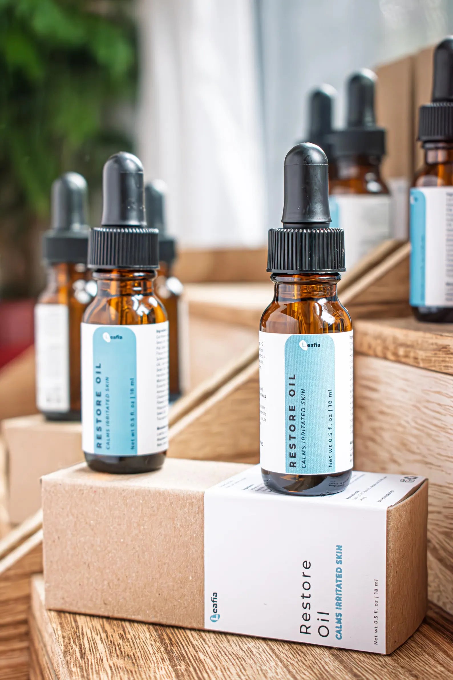 Leafia Skincare Restore Oil facial oil in amber dropper bottles with packaging on tiered wood blocks in soft natural light
