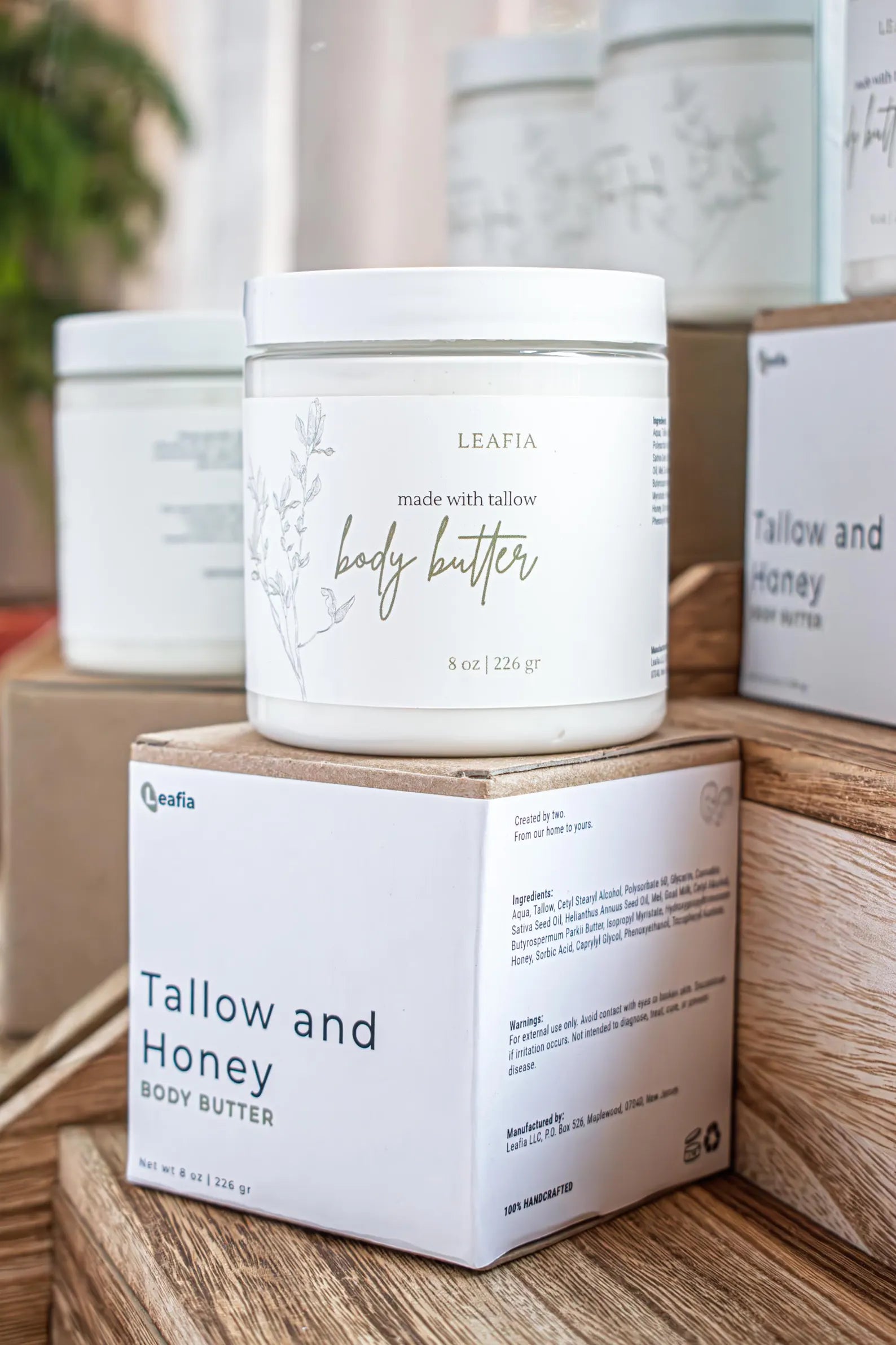 Leafia Skincare tallow body butter in white glass jar on kraft packaging atop rustic wood with warm apothecary light