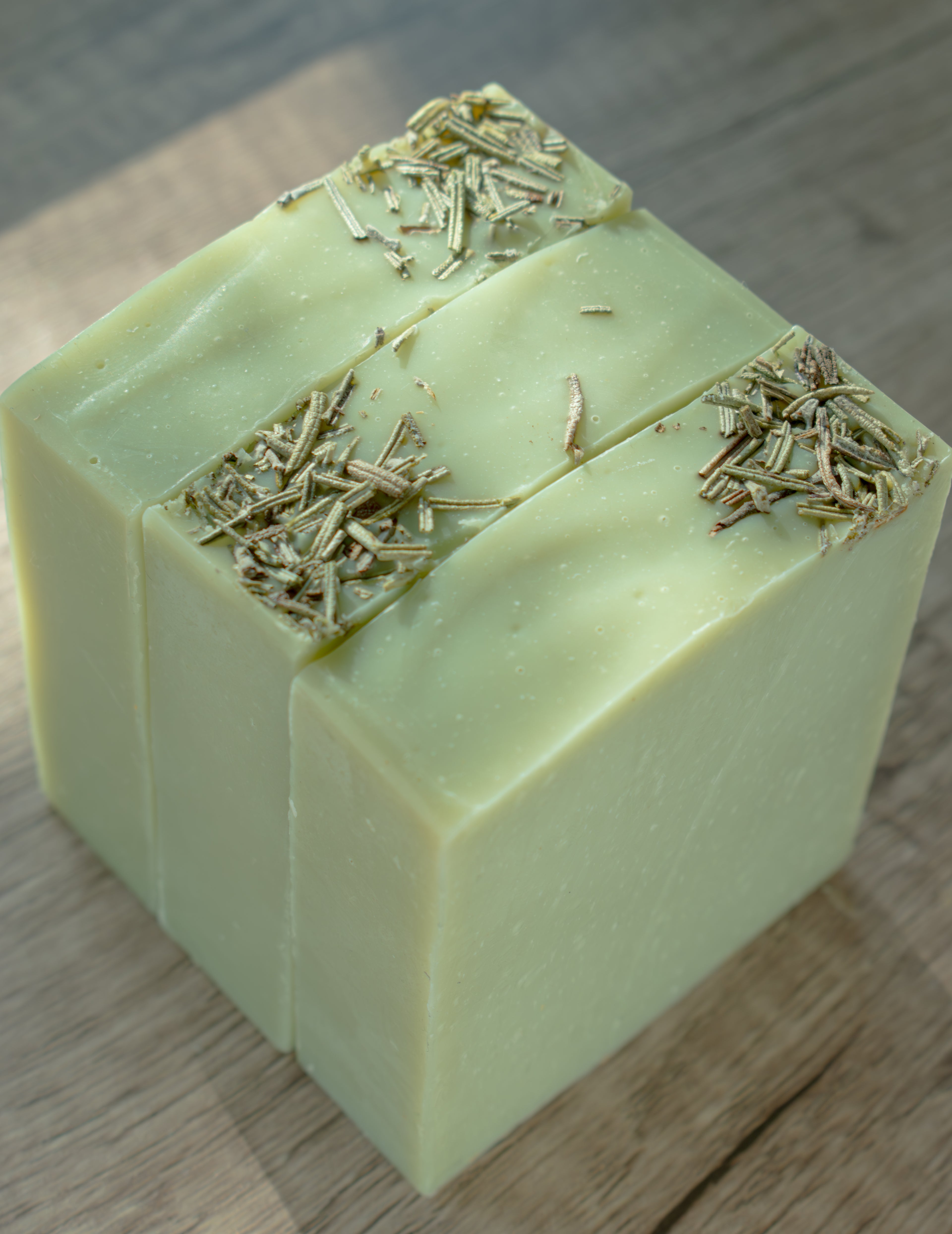 Three green soap bars with specks on a wooden surface