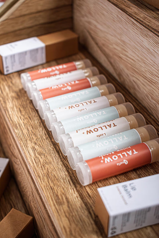 Leafia Skincare tallow lip balm tubes arranged on wooden surface, assorted label colors with minimal handmade packaging