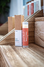 Leafia Skincare lip balm twist-up tube with kraft box on tiered wooden blocks under soft studio light