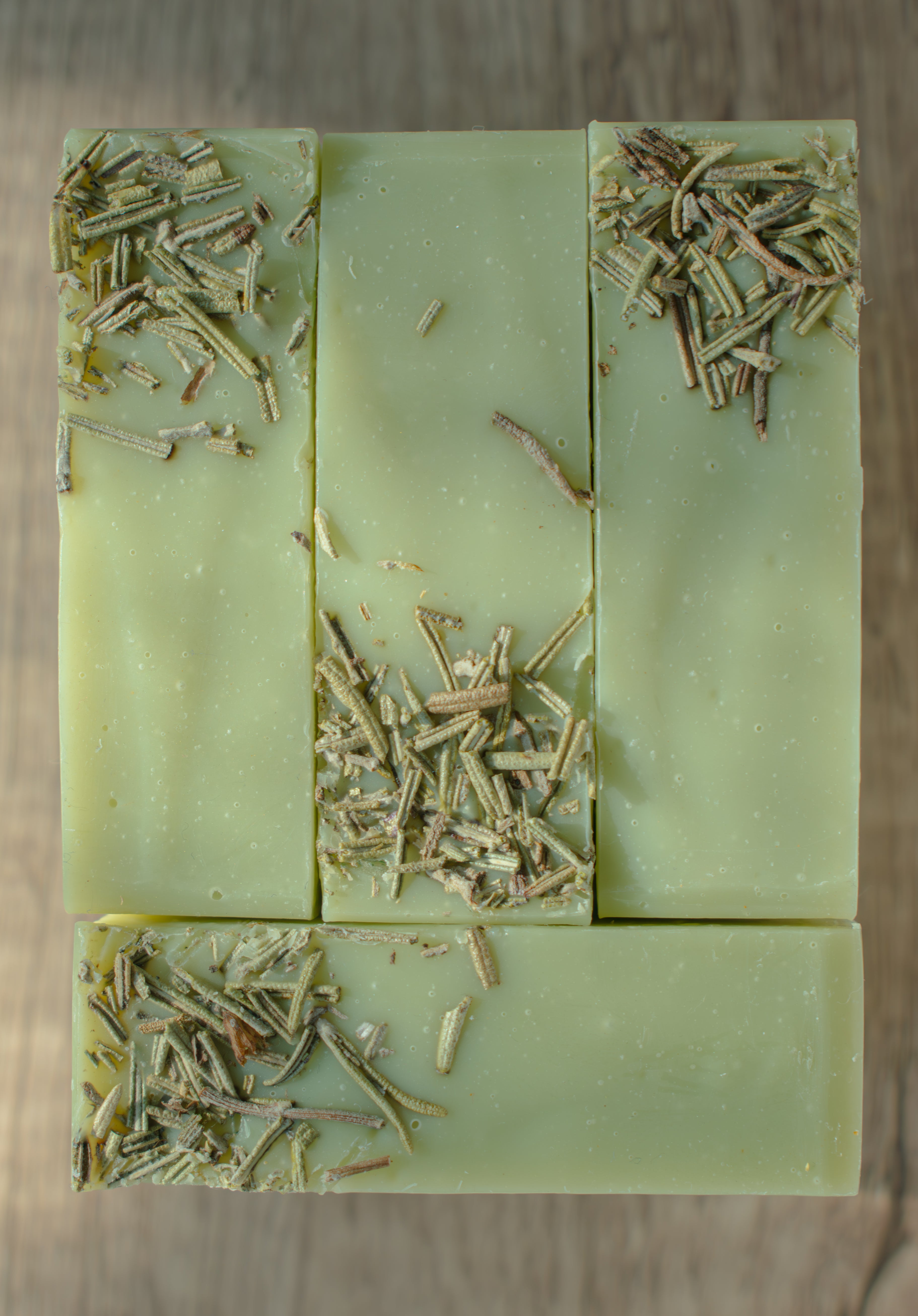Green soap bar with embedded herbs on a wooden surface