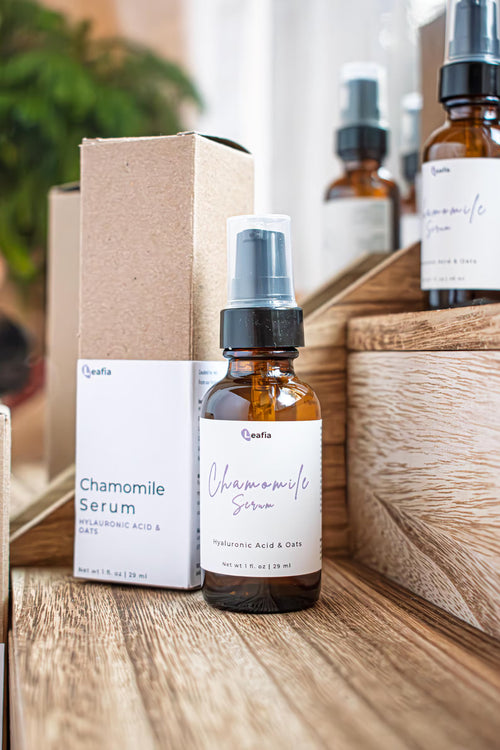 Leafia Skincare chamomile face serum in amber glass pump bottle beside kraft box on wooden surface in soft natural light