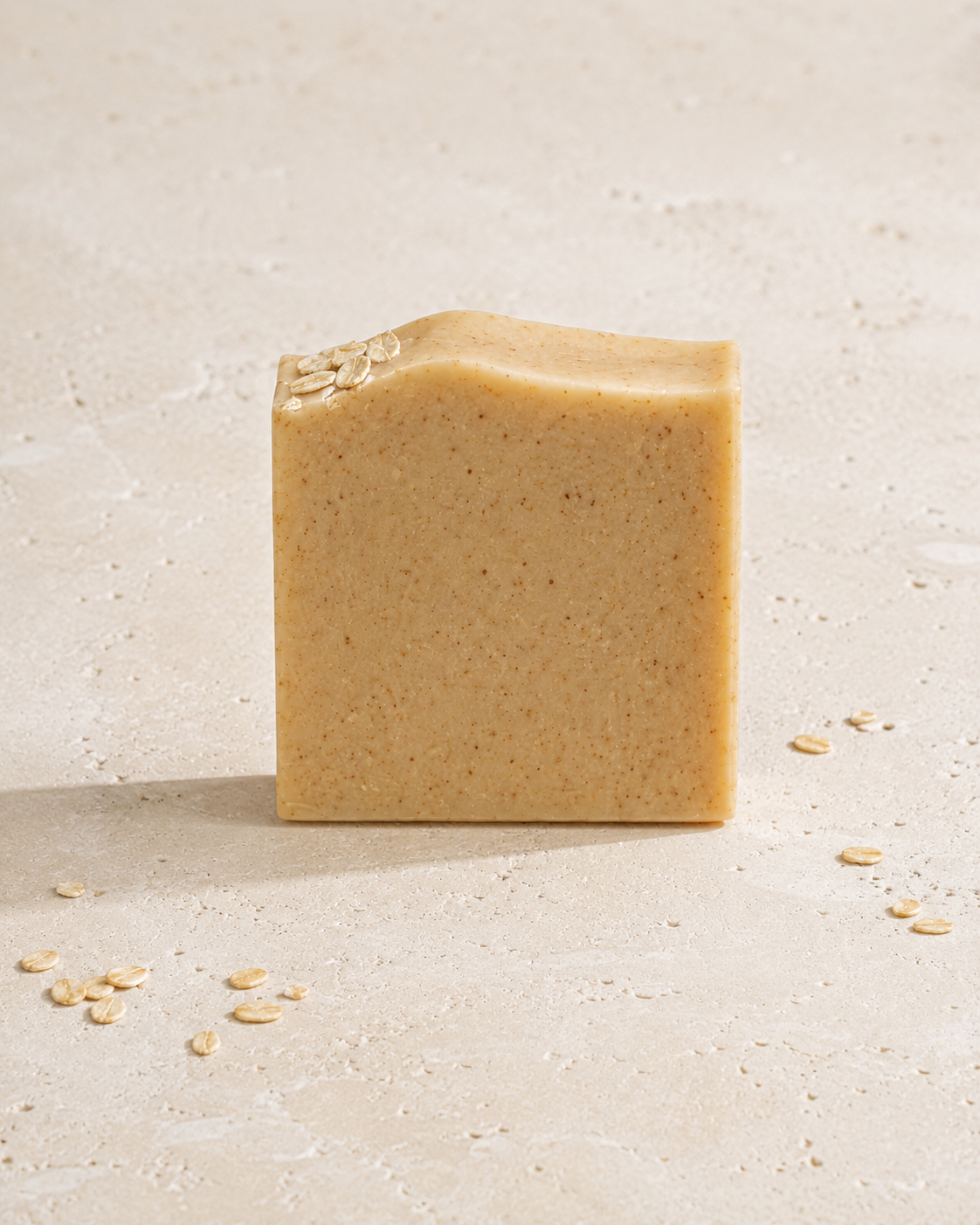 Bar of soap on a textured beige surface with scattered oats.