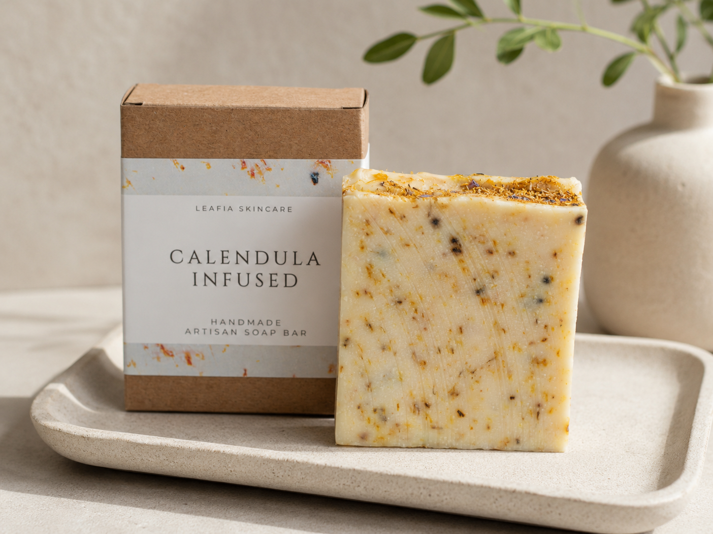 Calendula infused soap bar and packaging on a tray with a plant in the background