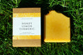 Orange soap on green grass. box label says honey, lemon, turmeric handmade artisan soap bar by leafia skincare