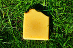 Orange soap on green grass. box label says honey, lemon, turmeric handmade artisan soap bar by leafia skincare