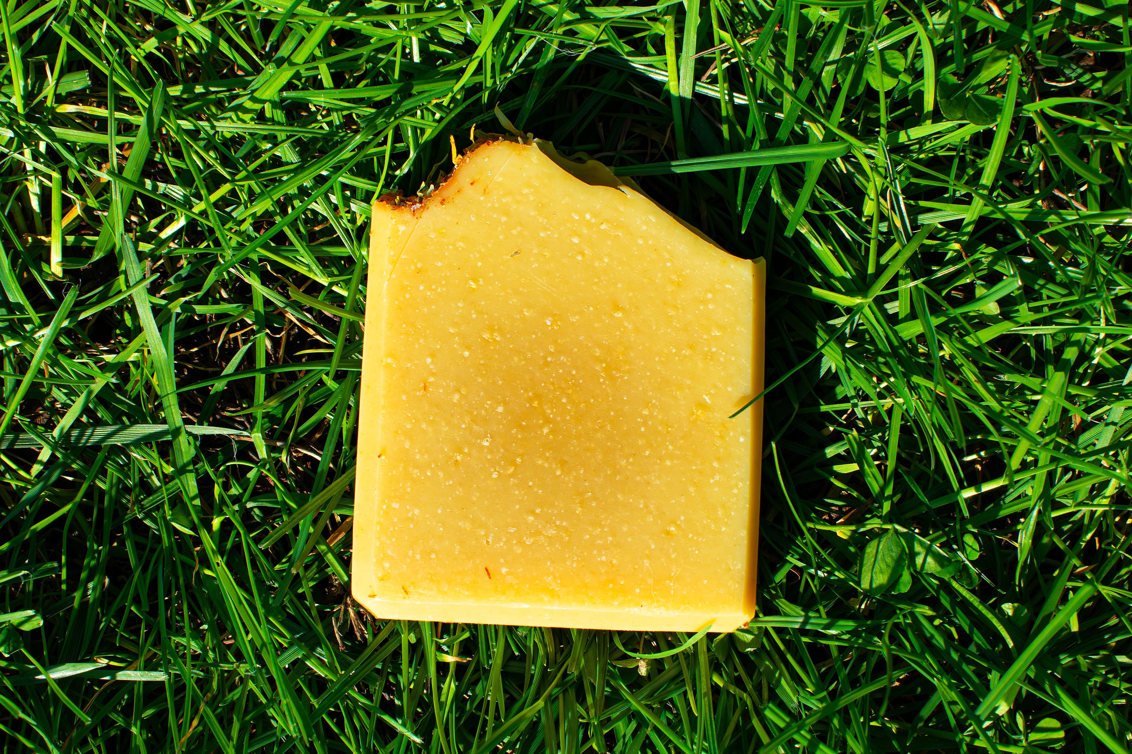 Orange soap on green grass. box label says honey, lemon, turmeric handmade artisan soap bar by leafia skincare
