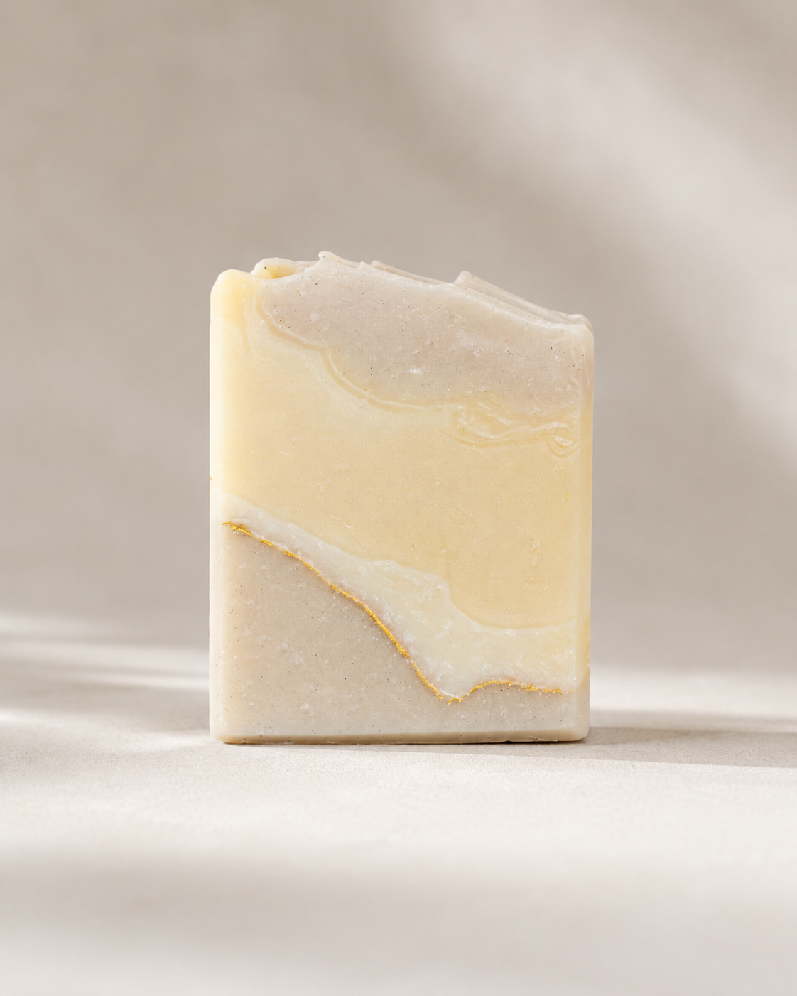 A single rectangular bar of handmade soap with a marbled pattern of cream, light yellow, and off-white, standing upright on a neutral beige surface with soft shadows.