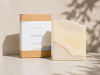 A bar of handmade artisan soap with a marbled cream and pale yellow pattern stands next to its kraft paper packaging box. The box features a white label with the brand name 'JUPITER' and 'LEAFIA SKINCARE' printed on it.