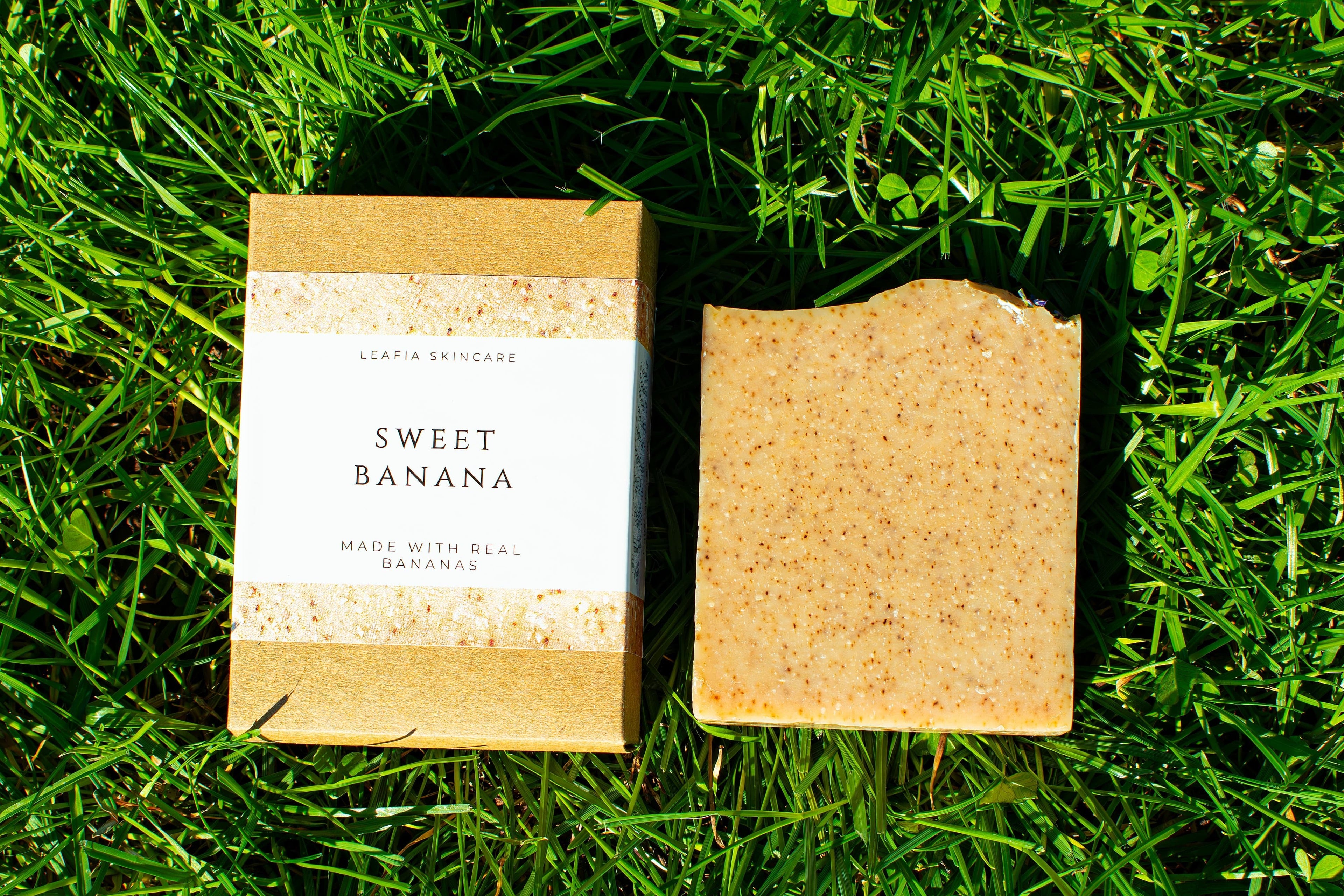Two soap bars on grass, one with a label 'Sweet Banana'.