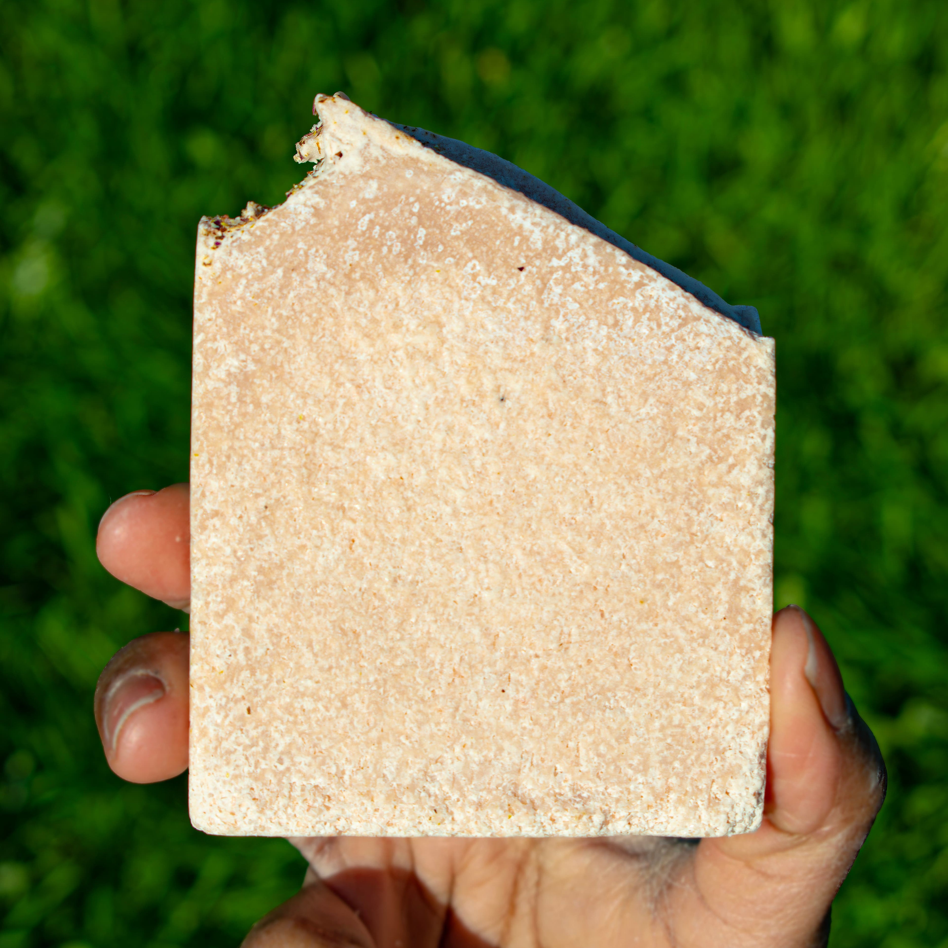 Hand holding a square piece of soap against a grassy background