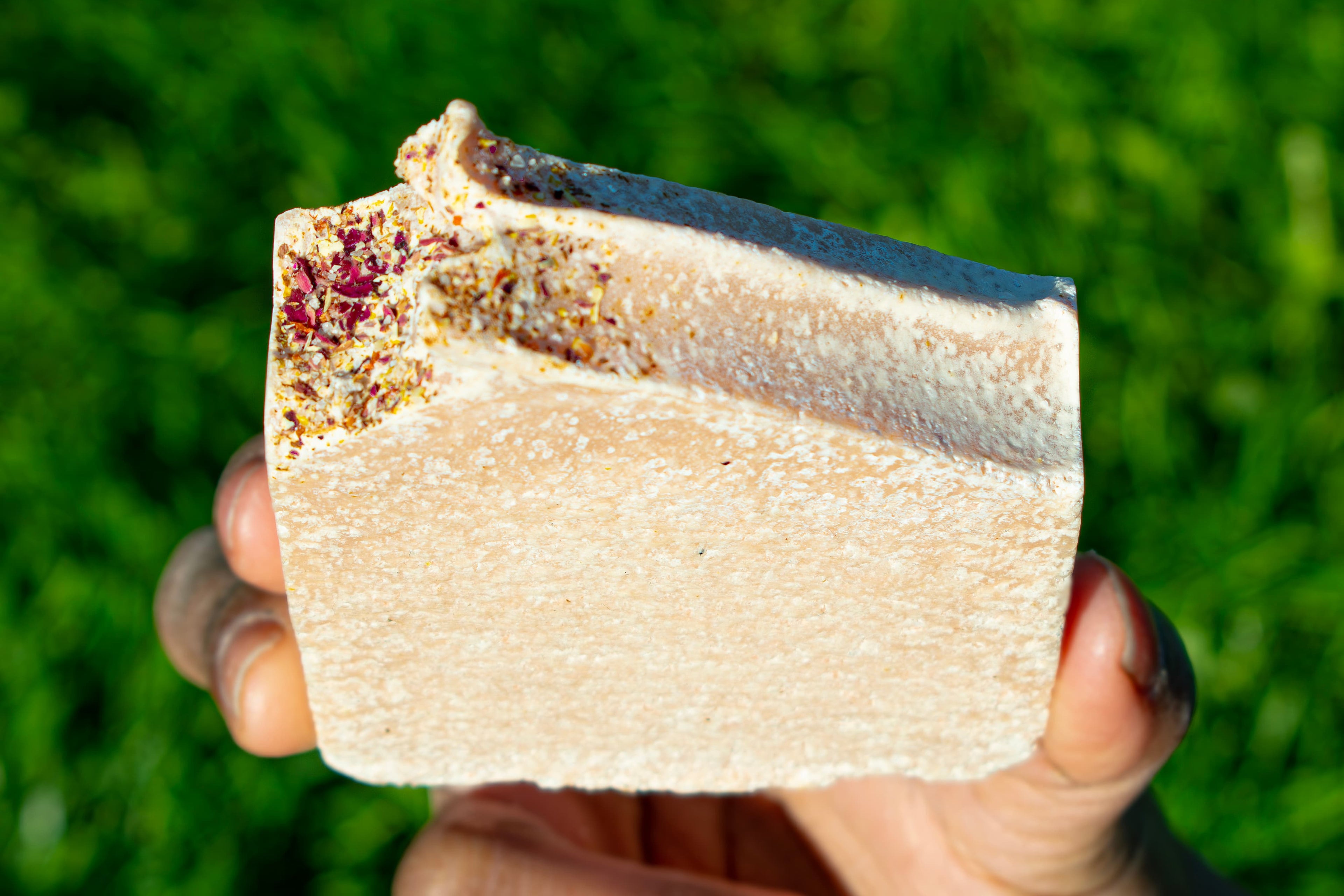 Hand holding a soap against a green grass background