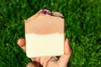 Hand holding a layered soap against a grassy background