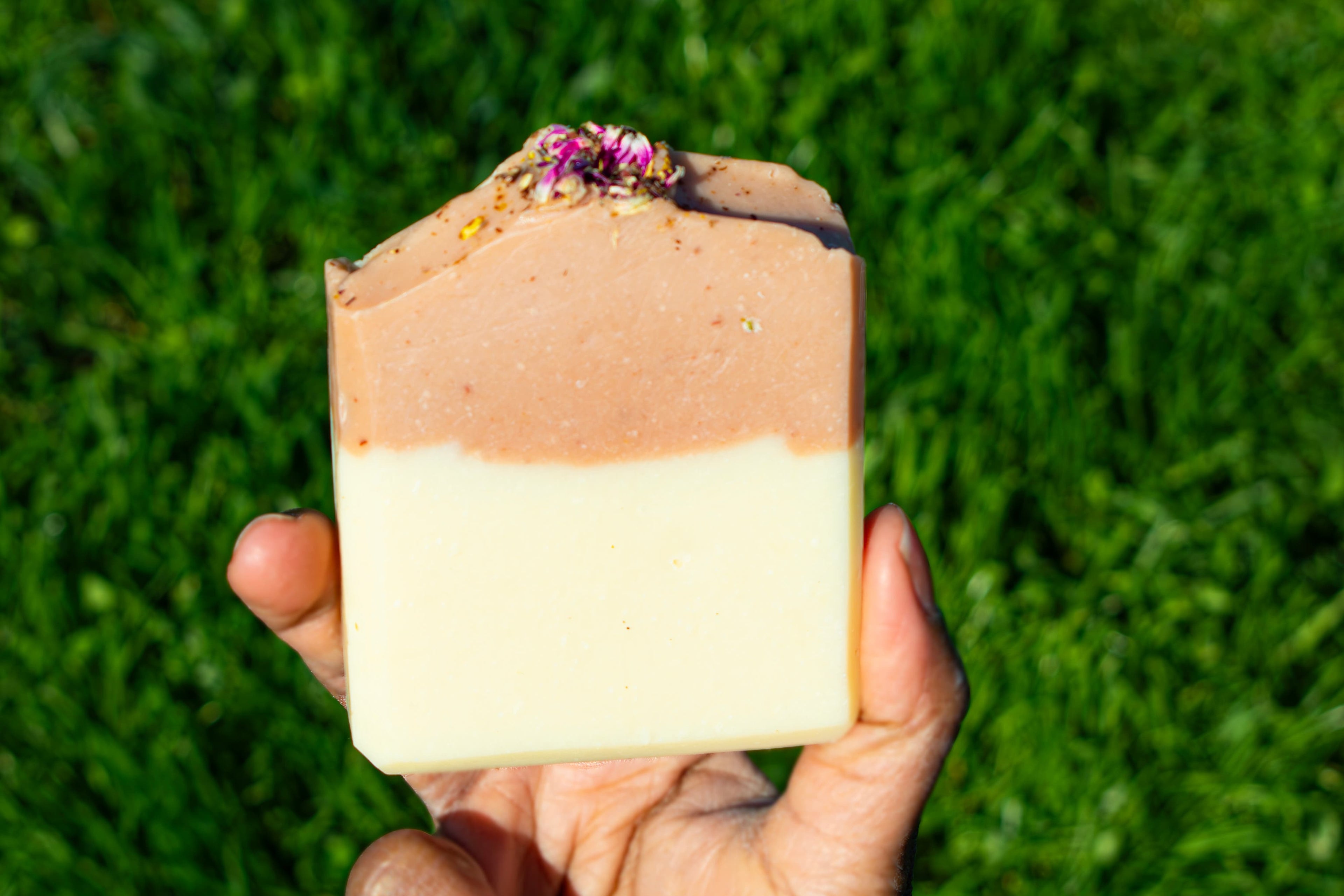 Hand holding a layered soap against a grassy background