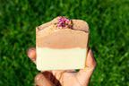 Hand holding a layered soap bar with a green grass background