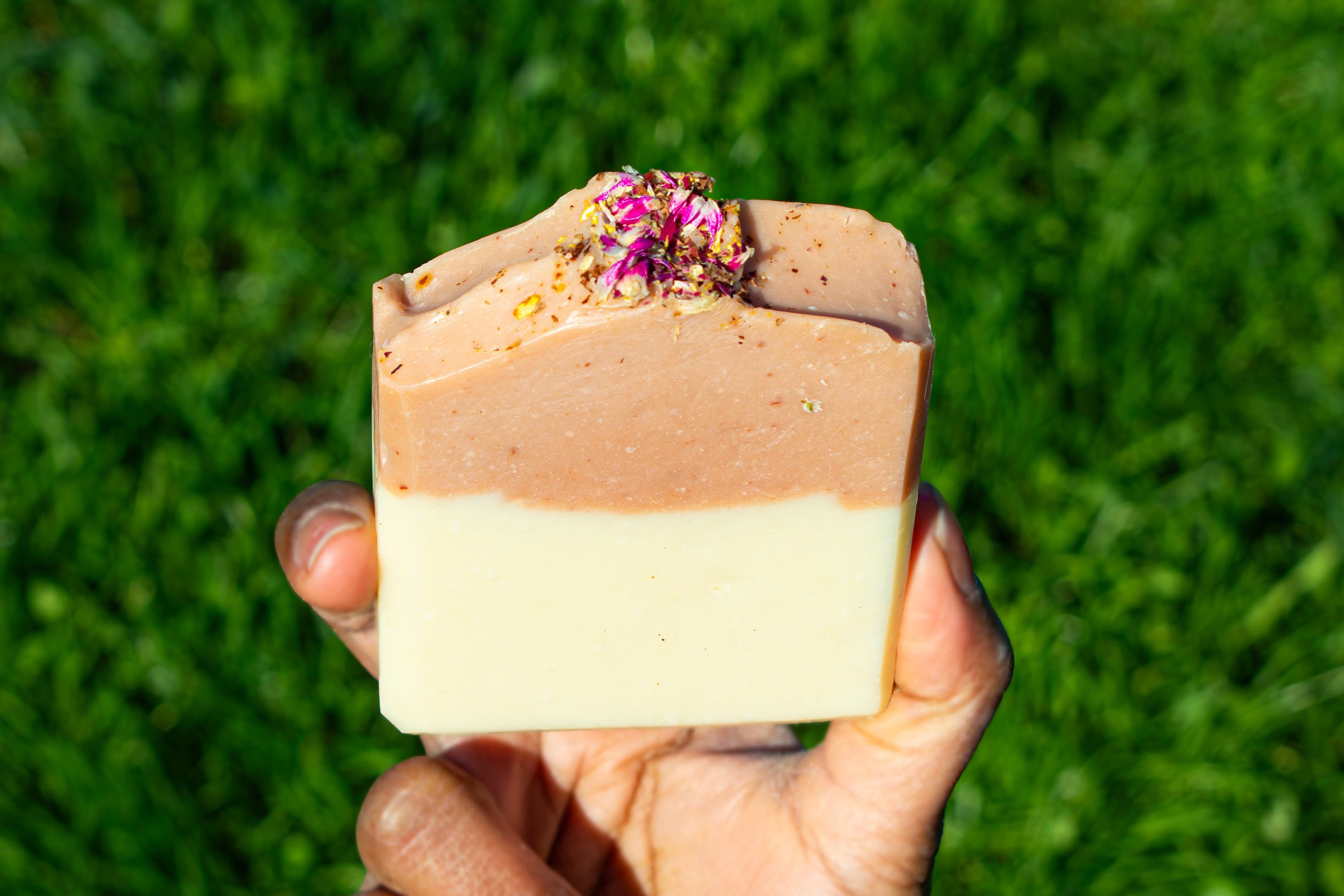 Hand holding a layered soap bar with a green grass background