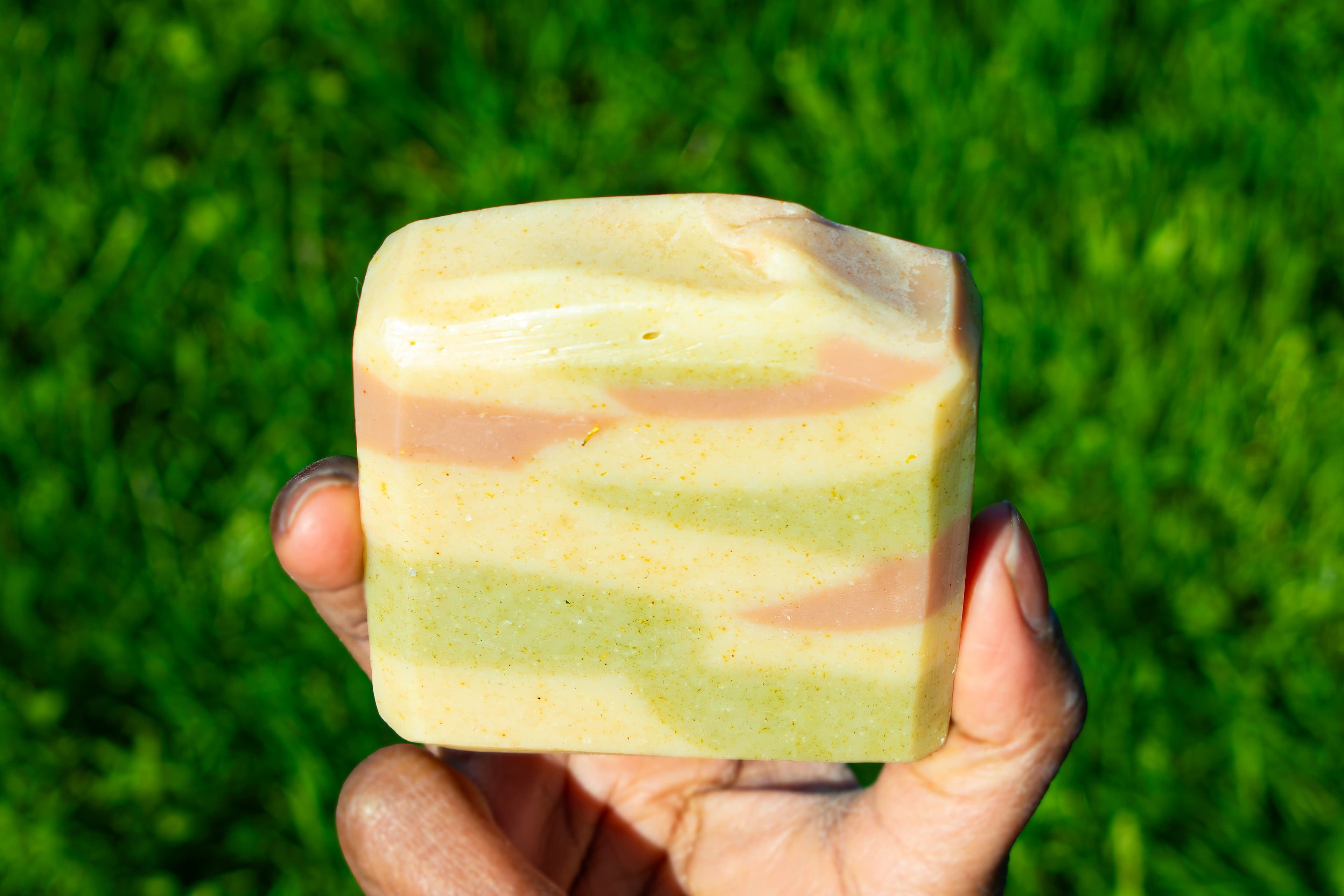 Hand holding a striped soap bar against a green grass background