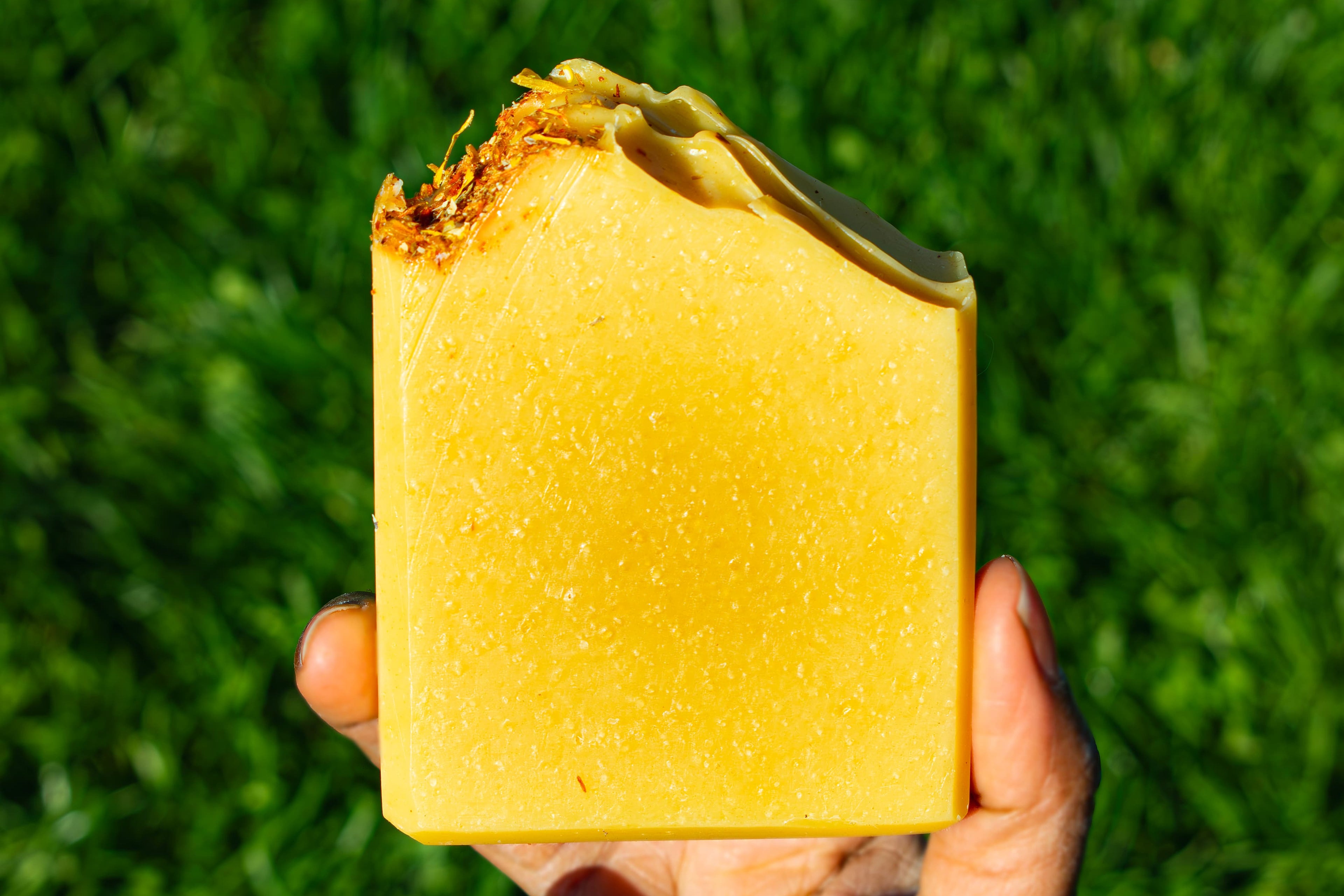Orange soap on green grass. box label says honey, lemon, turmeric handmade artisan soap bar by leafia skincare