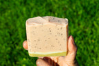 Hand holding a bar of soap against a grassy background