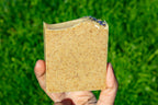 Hand holding a square piece of soap against a grass background