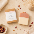 Rose rice water soap bar with packaging on a textured surface with dried rose petals.