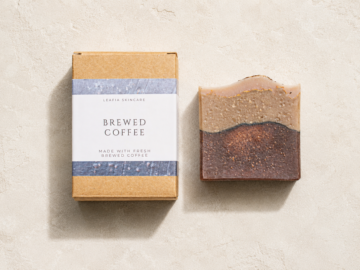 Bar of coffee-scented soap next to its packaging on a beige background